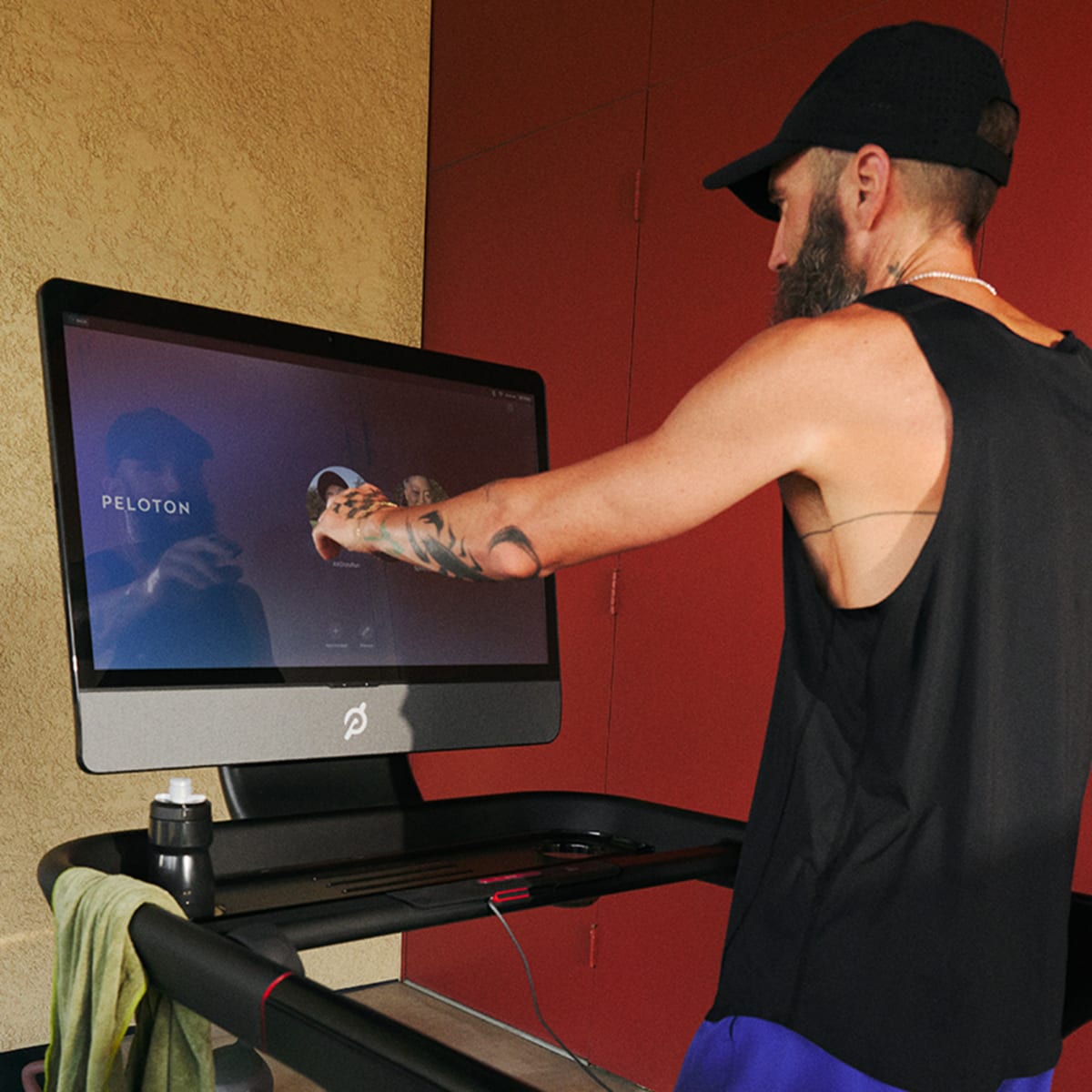 A man running on the Peloton Tread touching the screen.