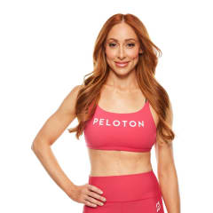 A headshot of Peloton instructor Jess King. She's smiling with one hand on her hip. She's wearing a pink Peloton sports bra.